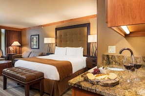Hotelkamer met een groot bed, een houten hoofdeinde, een marmeren aanrecht met eten en wijn, en een bank.