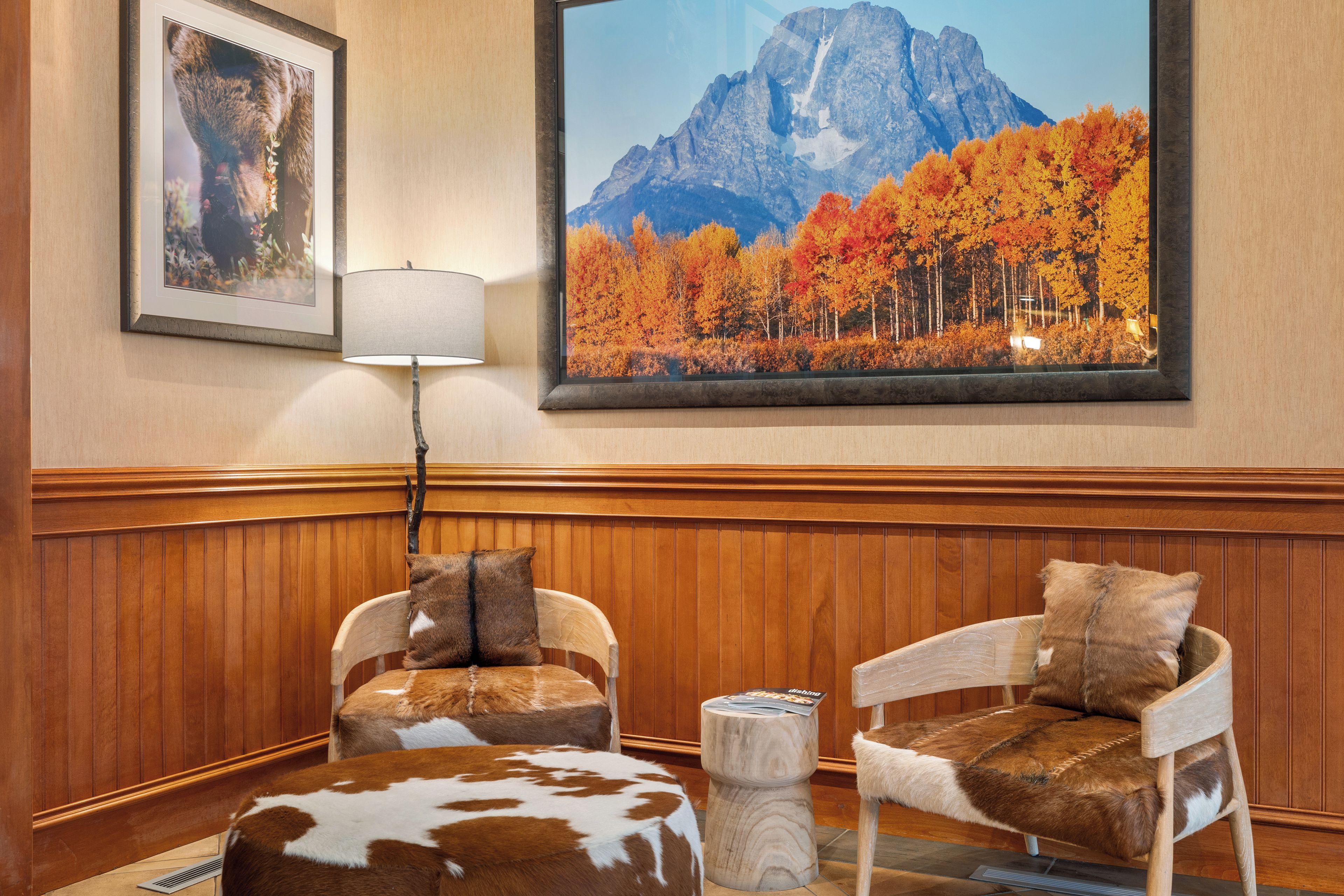 Una habitación con dos sillones tapizados en imitación piel, un banco de madera y un cuadro con un paisaje montañoso.