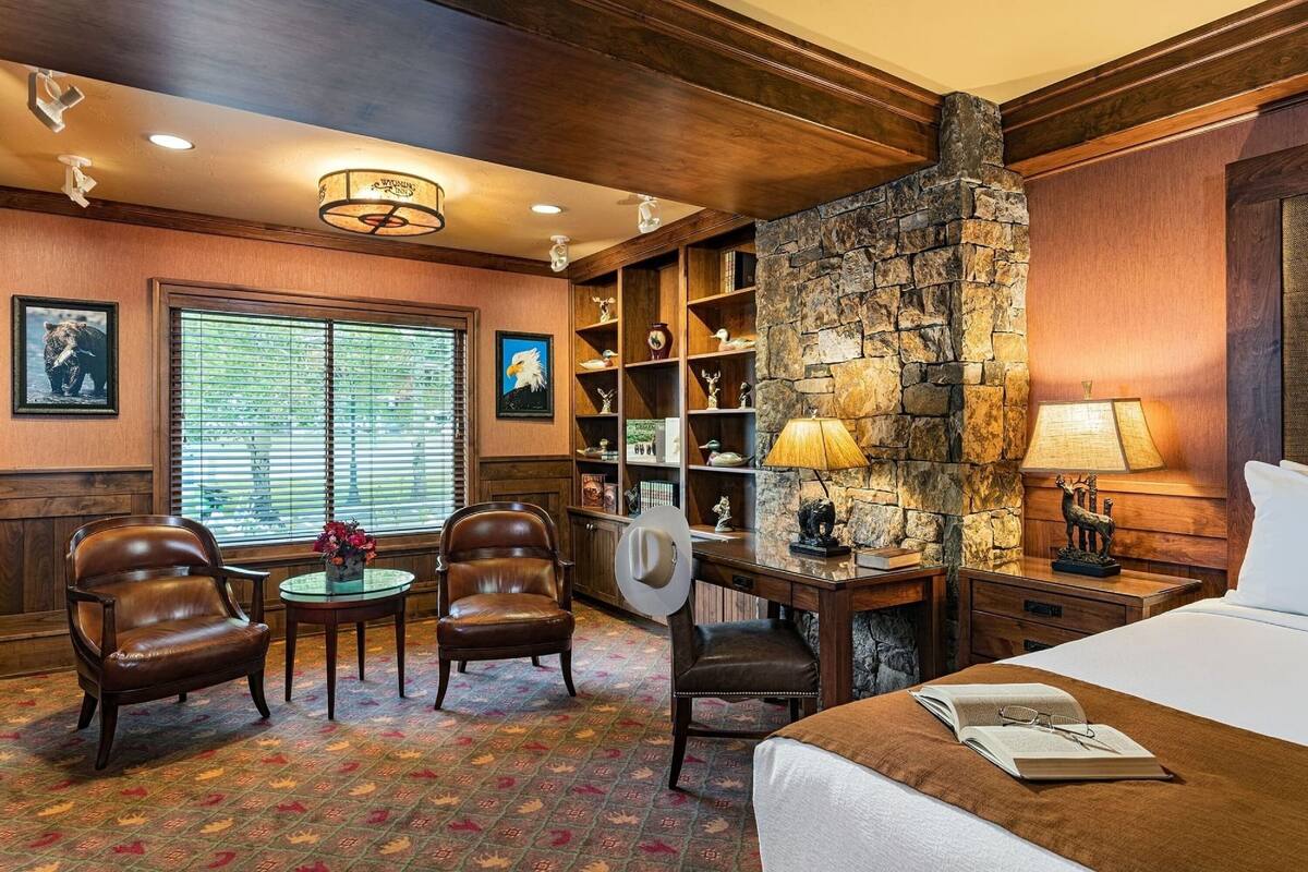 A hotel room with a stone fireplace, wooden shelves, a desk, and a bed.