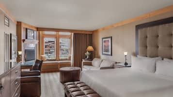 Een hotelkamer met een groot bed, een bureau met stoel, een bank, een klein rond voetenbankje, een televisie en een raam met gordijnen.