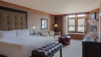A hotel room with a large bed, a bench, a desk, and a fireplace.