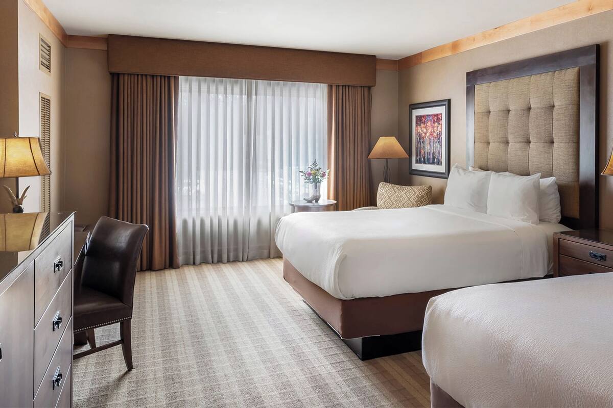 A hotel room with a large bed, a smaller bed, a desk, a chair, and a dresser.