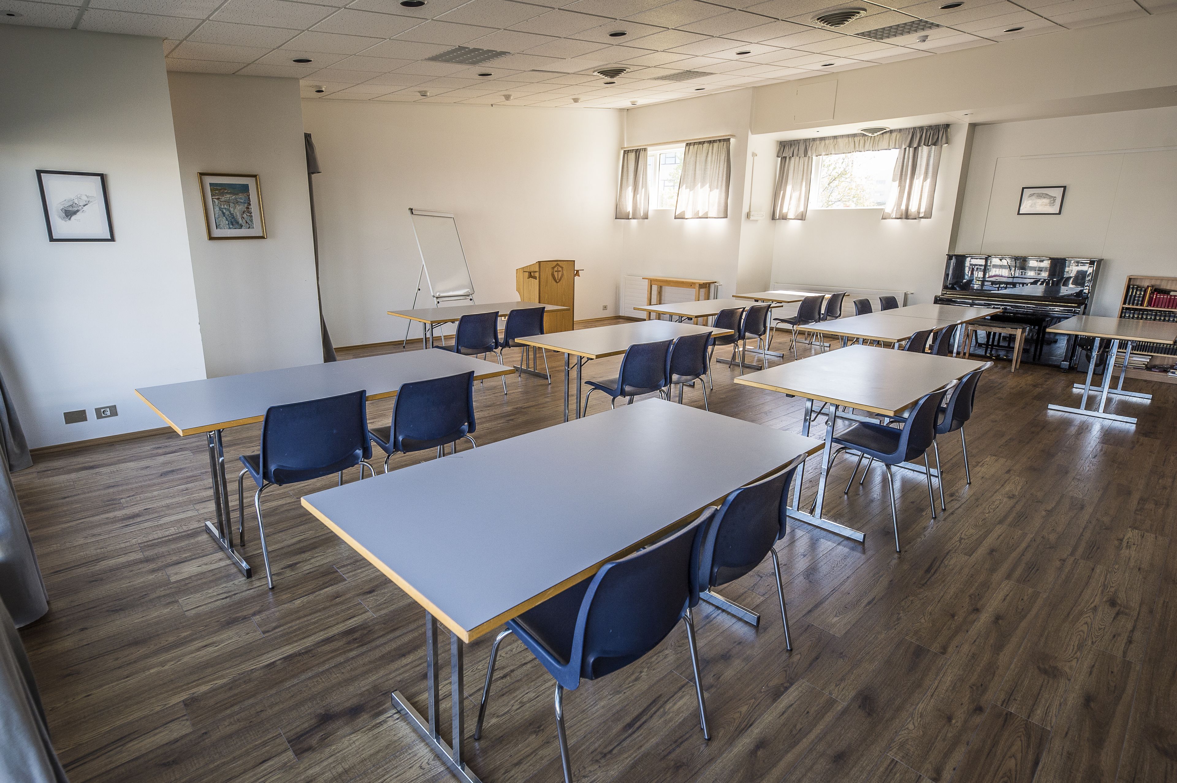 A classroom with wooden desks and chairs, a whiteboard, and a projector screen.