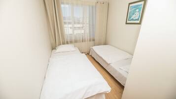 A small, clean room with two single beds, a window with sheer curtains, and a framed picture on the wall.