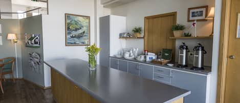 A modern kitchen with a central island, wooden cabinets, and a small dining area with a chair.