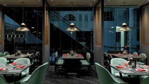 Ein modernes Restaurant mit mehreren Essplätzen, grünen Stühlen und Pendelleuchten.