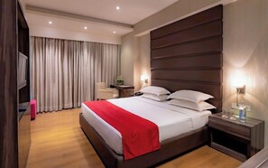 A hotel room with a large bed, a desk, a chair, and a TV.