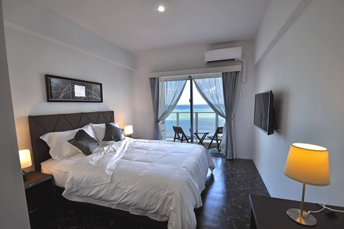 Une chambre d’hôtel avec un lit, une télévision, une lampe et une vue sur la mer par la fenêtre.
