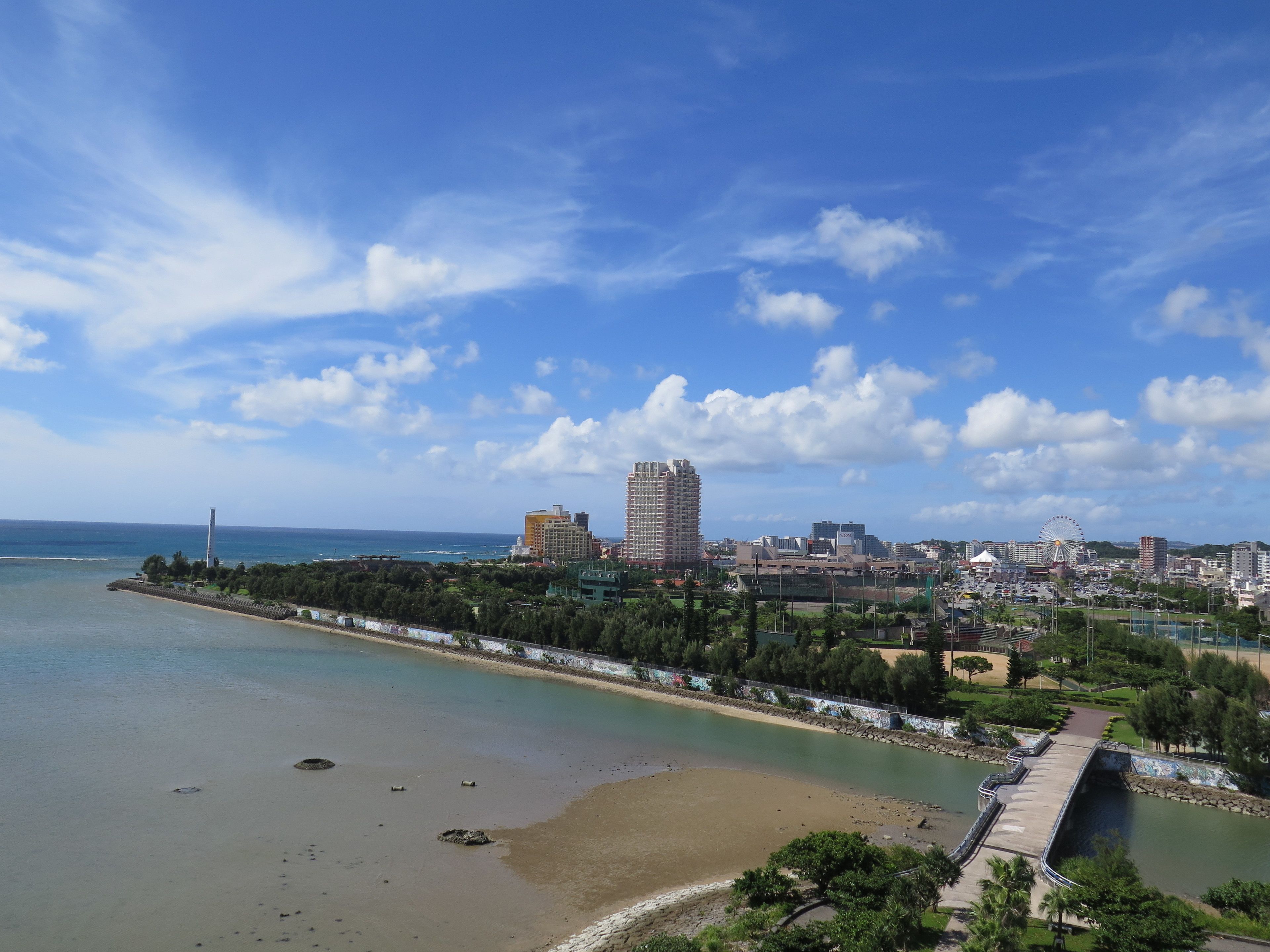 Eine Küstenstadtlandschaft mit Strand, einem Steg und einem Riesenrad in der Ferne.