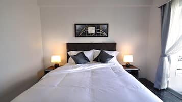 Una cama bien hecha con sábanas blancas y dos almohadas negras, flanqueada por dos mesitas de noche con lámparas, en una habitación con cabecera oscura y una obra de arte abstracta enmarcada sobre la cama.
