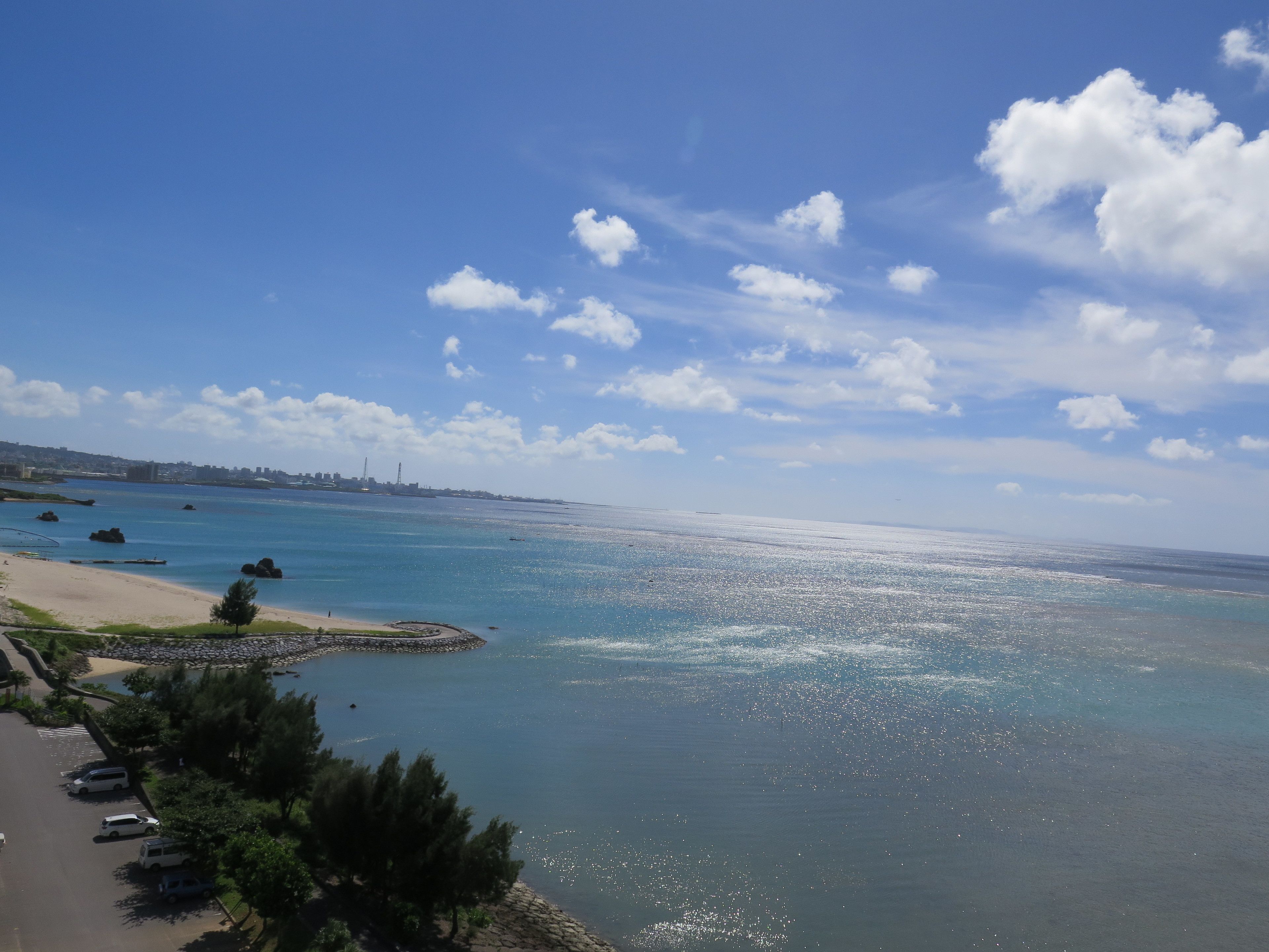 Vista costera con playa de arena, zona de estacionamiento y cielo despejado.
