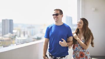 A man and woman standing on a balcony with a cityscape view.