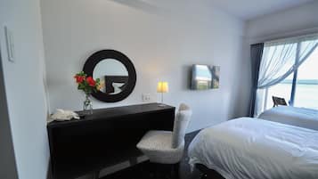 A hotel room with a bed, a desk with a mirror, a chair, a TV, and a window with curtains.