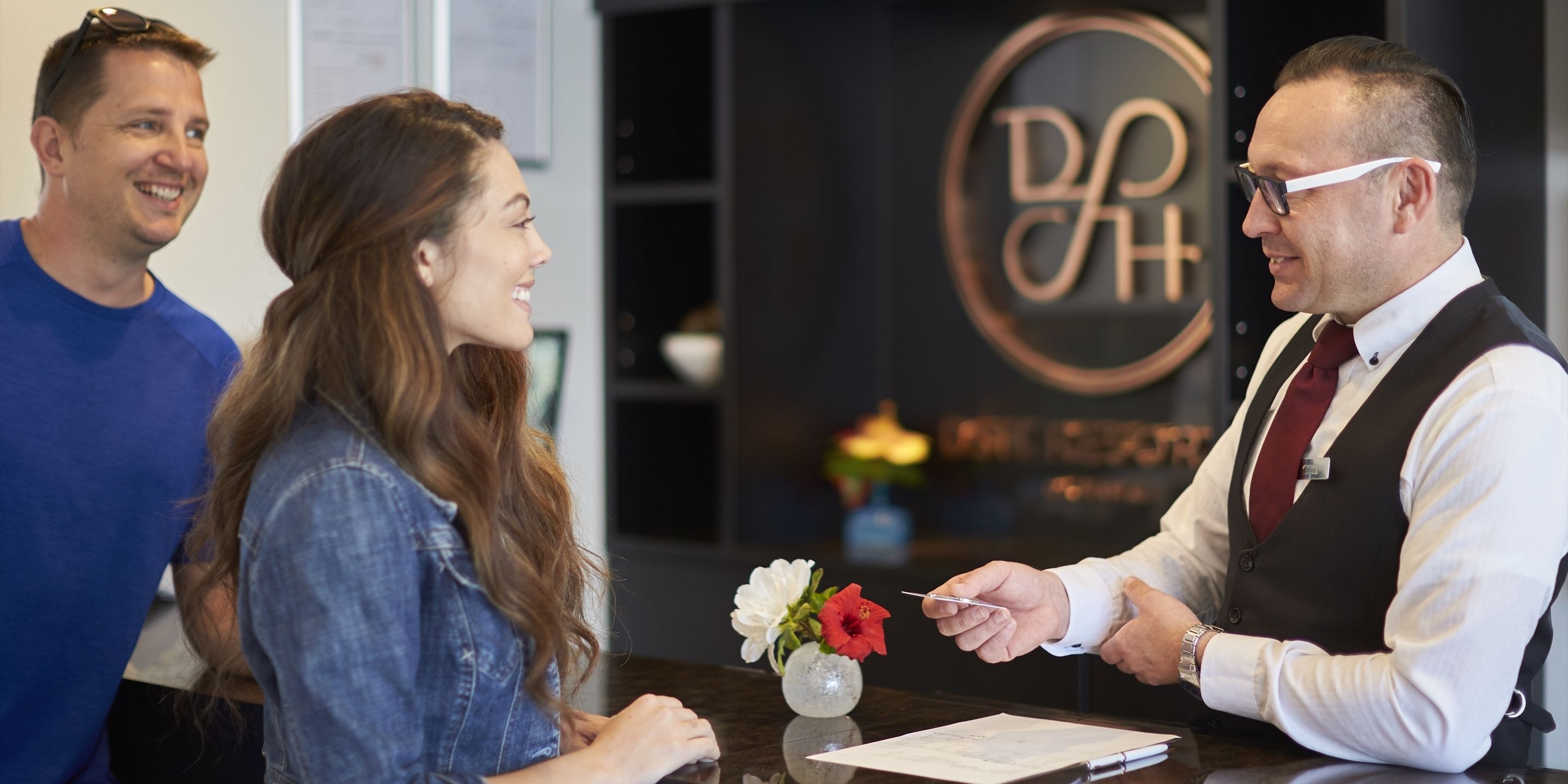 A reception desk with a logo, a vase with flowers, and a menu or information card.