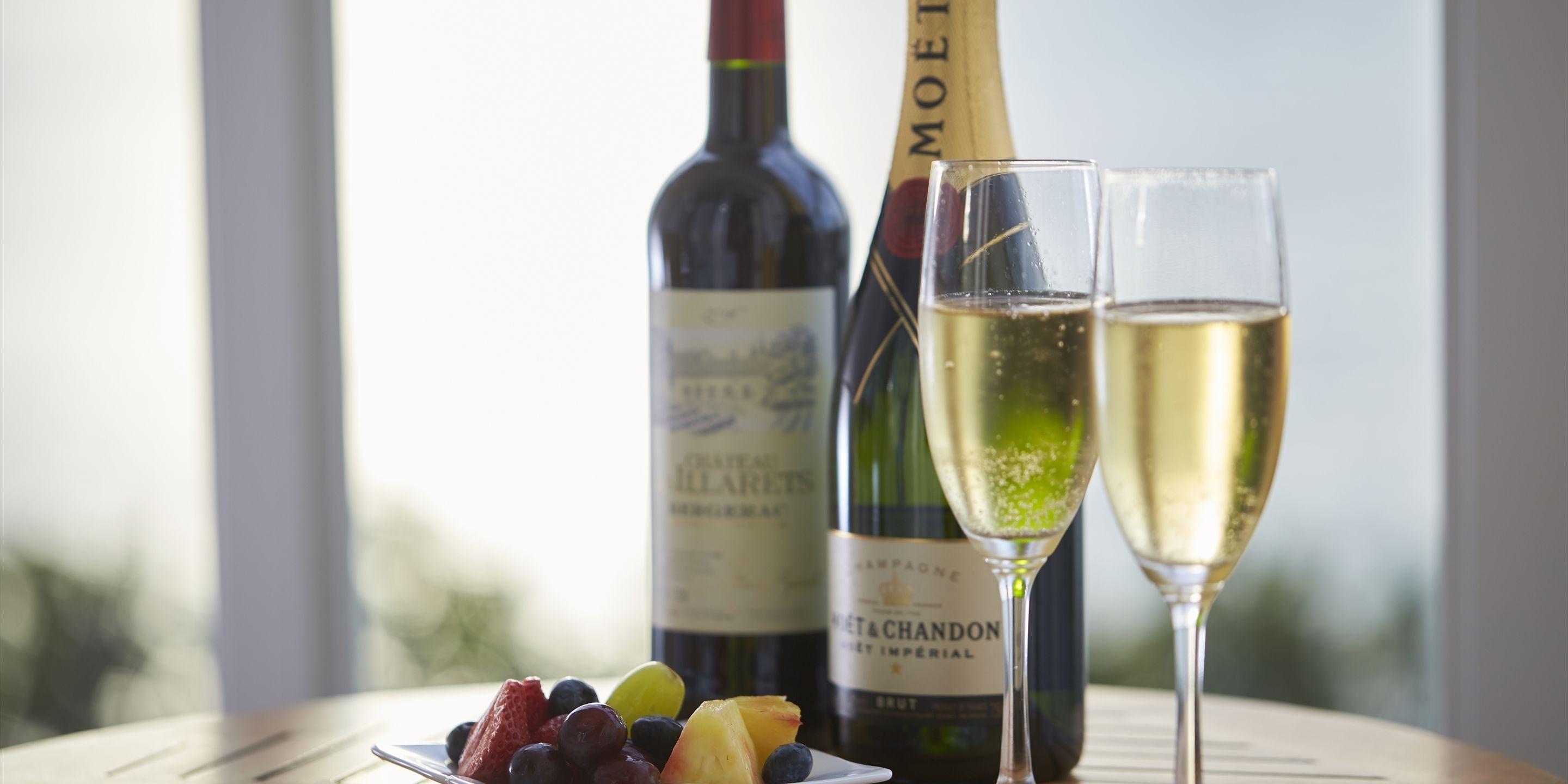 A table with a bottle of wine, two glasses of champagne, and a plate of fruit.