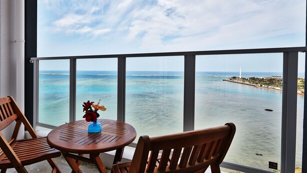 Un balcon avec vue sur la mer, une table ronde en bois ornée d’un vase de fleurs et deux chaises en bois.