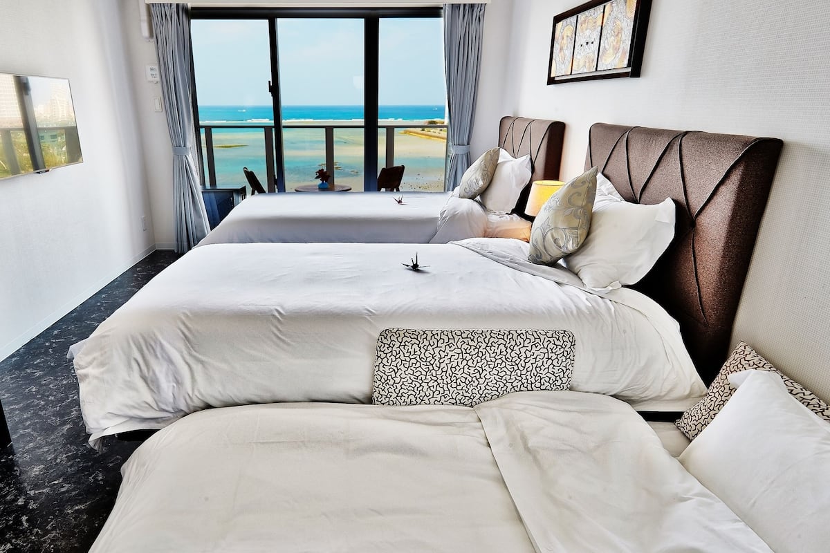 Une chambre d’hôtel avec deux lits, une télévision, un bureau et vue sur la plage.