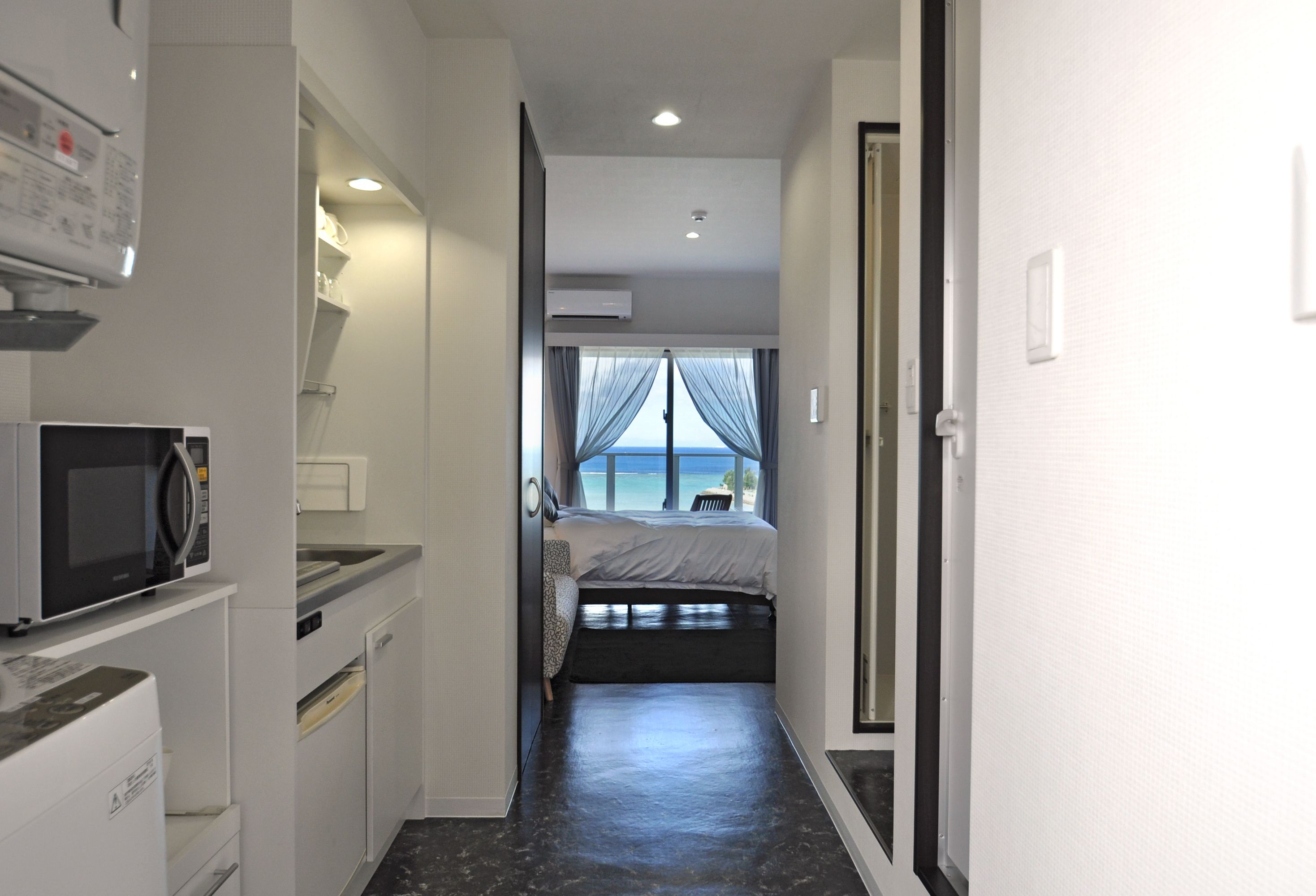 Un pasillo estrecho que conduce a un dormitorio con cama, microondas, lavabo y aire acondicionado.