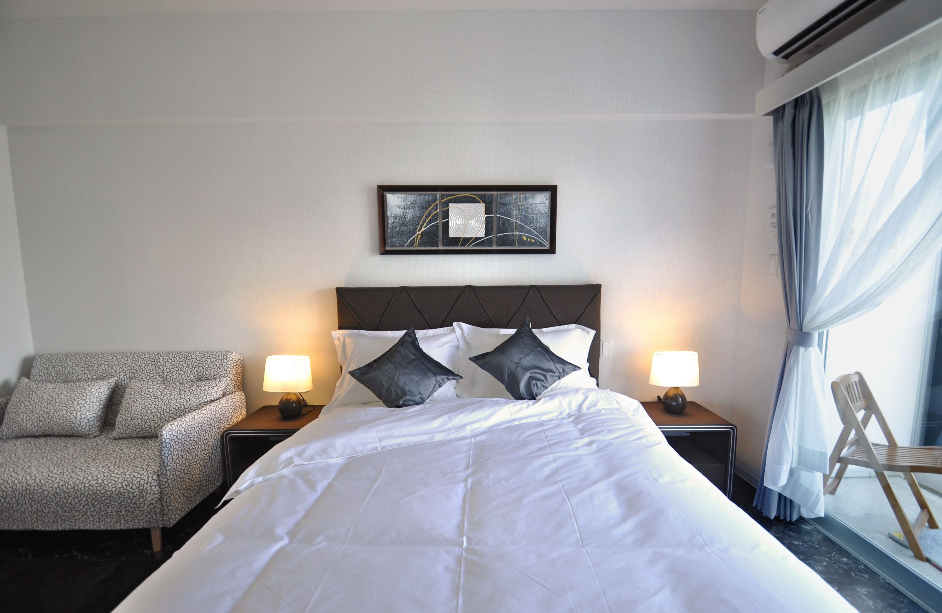 A hotel room with a large bed, two bedside lamps, a chair, and a window with curtains.