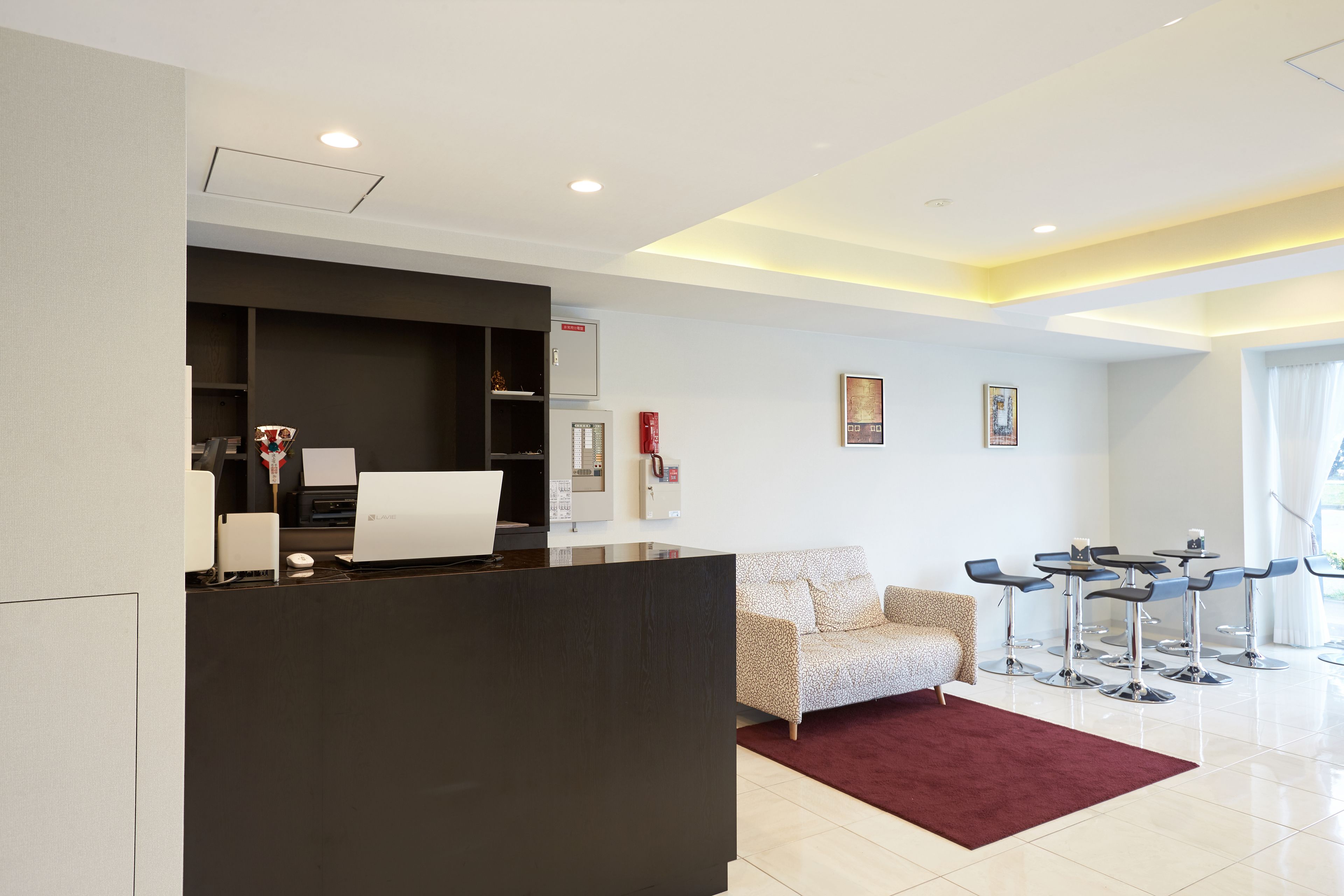 Una moderna area reception con una scrivania scura, un divano a fantasia e un angolo salotto con tavoli e sedie.
