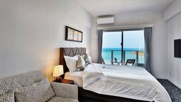 A hotel room with a bed, a sofa, a TV, and a balcony with a view of the sea.