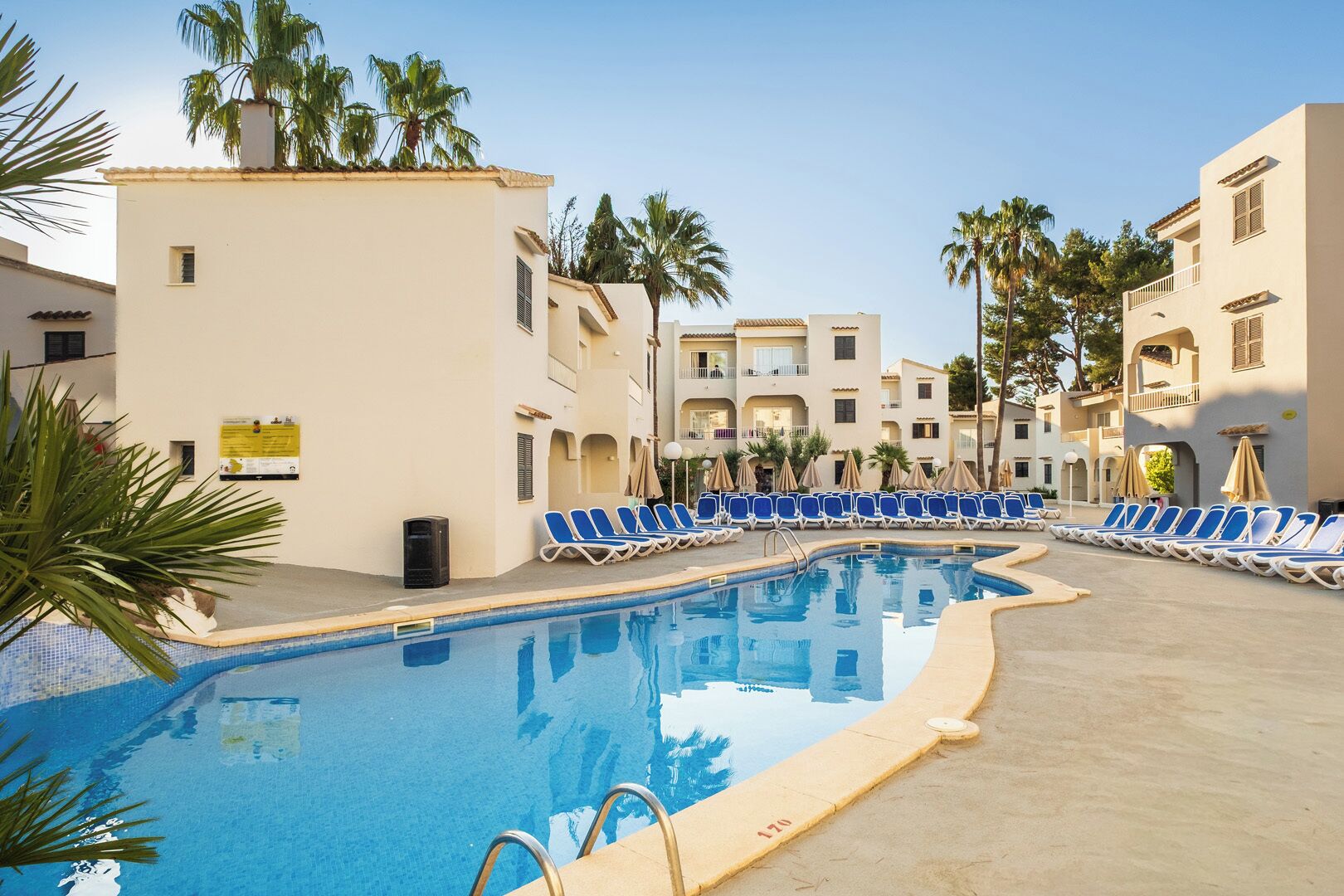 A swimming pool with lounge chairs and palm trees, surrounded by multi-story buildings.