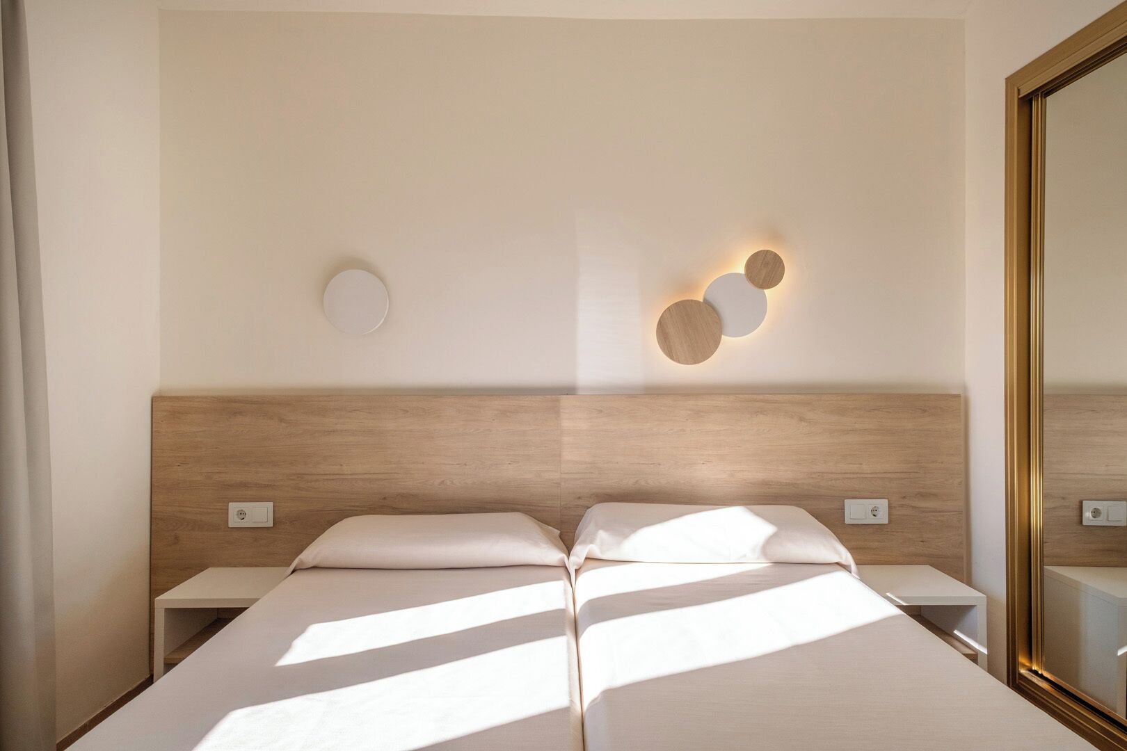 A hotel room with a wooden headboard, two bedside tables, and a wall-mounted light fixture.