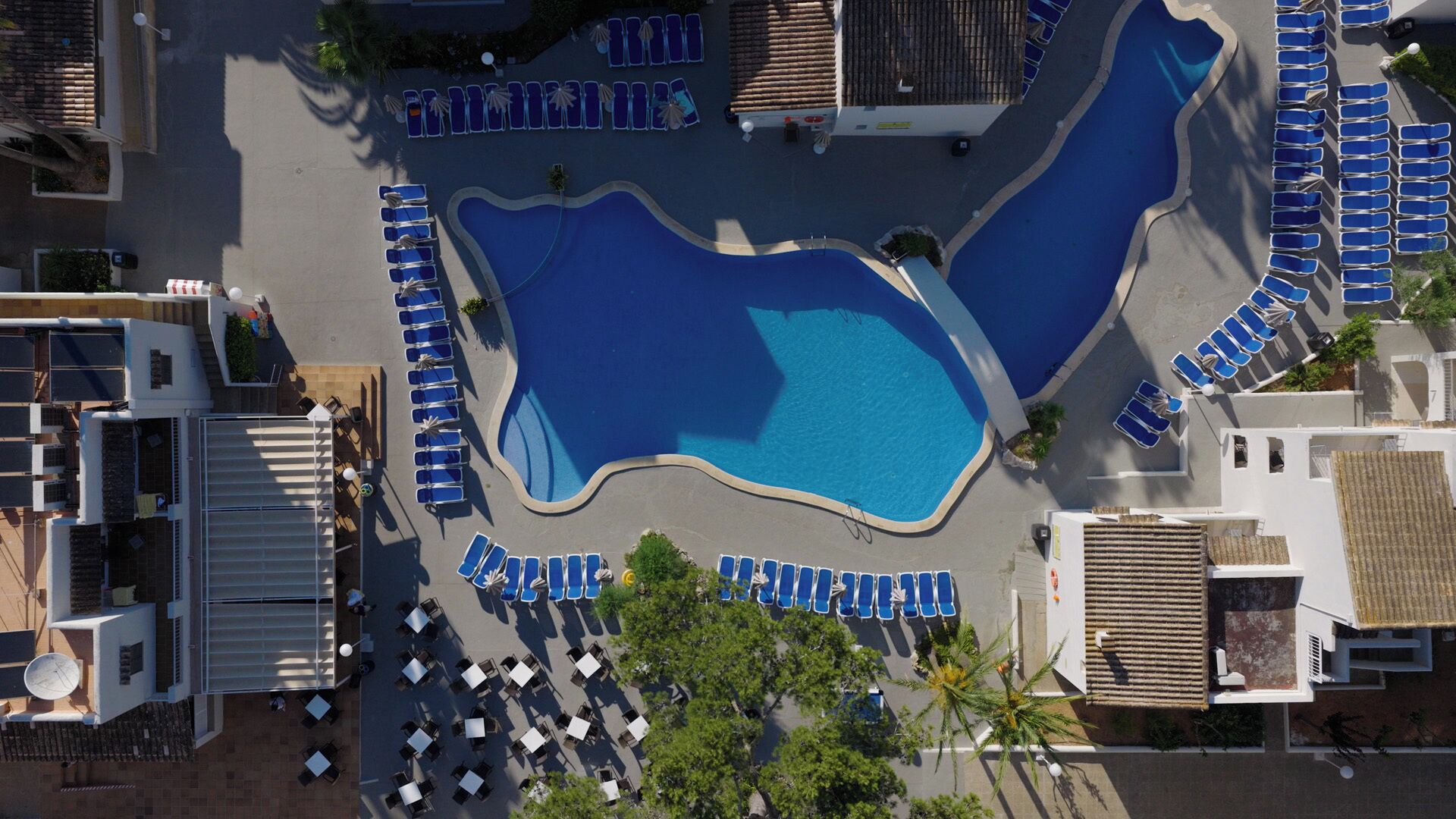 An aerial view of a resort with multiple swimming pools, sun loungers, and outdoor seating areas.