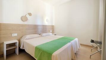 Una habitación de hotel con cama, mesitas de noche, lámpara de pared y una silla.