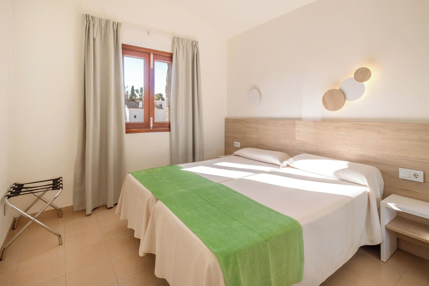 Ein Hotelzimmer mit Bett, Sessel, Fenster mit Vorhängen und Wandleuchte.