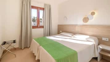 Habitación de hotel con cama, una silla, ventana con cortinas y lámpara de pared.