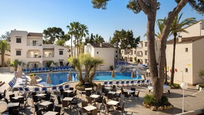 A pool area with lounge chairs and tables, surrounded by palm trees and buildings. - Cabot Club Torre Blanca (Sant Llorenc des Cardassar)