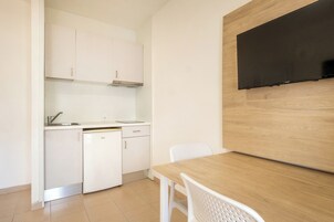 Cocina compacta con armarios blancos, lavavajillas y una mesa de comedor de madera con dos sillas.