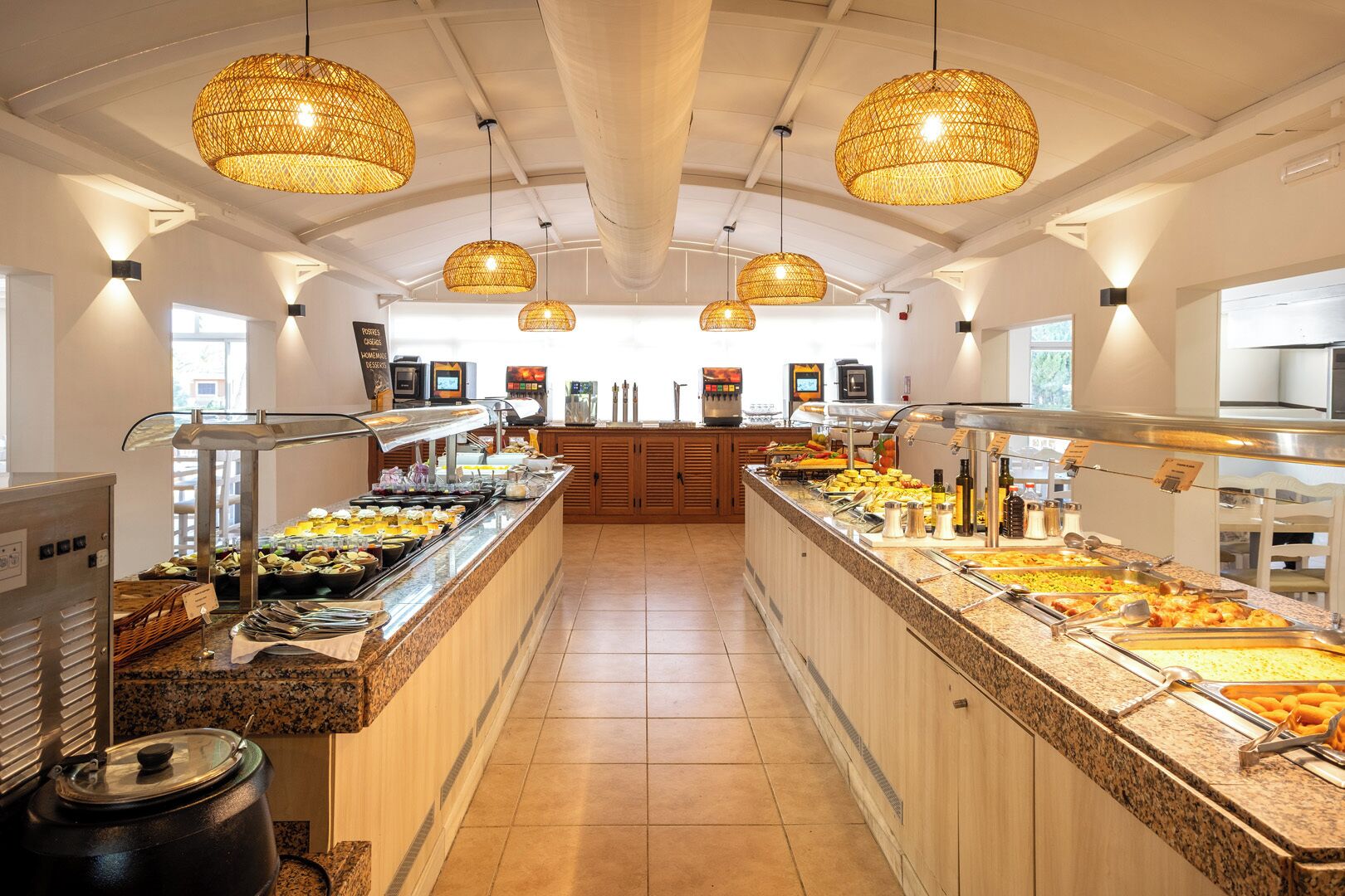 Zona de buffet con varias estaciones de comida, iluminación de mimbre colgante y un mostrador central de servicio.