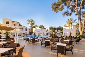 An outdoor pool area with lounge chairs and tables, surrounded by buildings and trees. - Cabot Club Torre Blanca (Sant Llorenc des Cardassar)