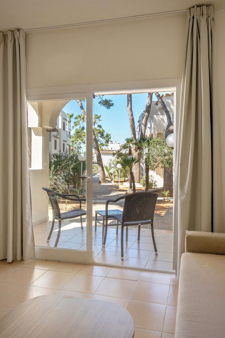 Una habitación con puerta corrediza de vidrio que da a un espacio exterior con sillas y palmeras.