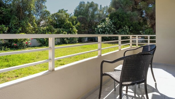 A balcony with a white railing, a wicker chair, and a view of a grassy area with trees. - Cabot Club Torre Blanca (Sant Llorenc des Cardassar)