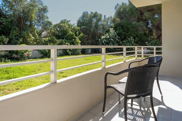 A balcony with a white railing, a wicker chair, and a view of a grassy area with trees. - Cabot Club Torre Blanca (Sant Llorenc des Cardassar)