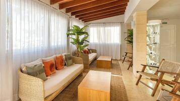 Una sala de estar con un sofá, una mesa de centro y sillas, una planta grande y una vitrina de vidrio.