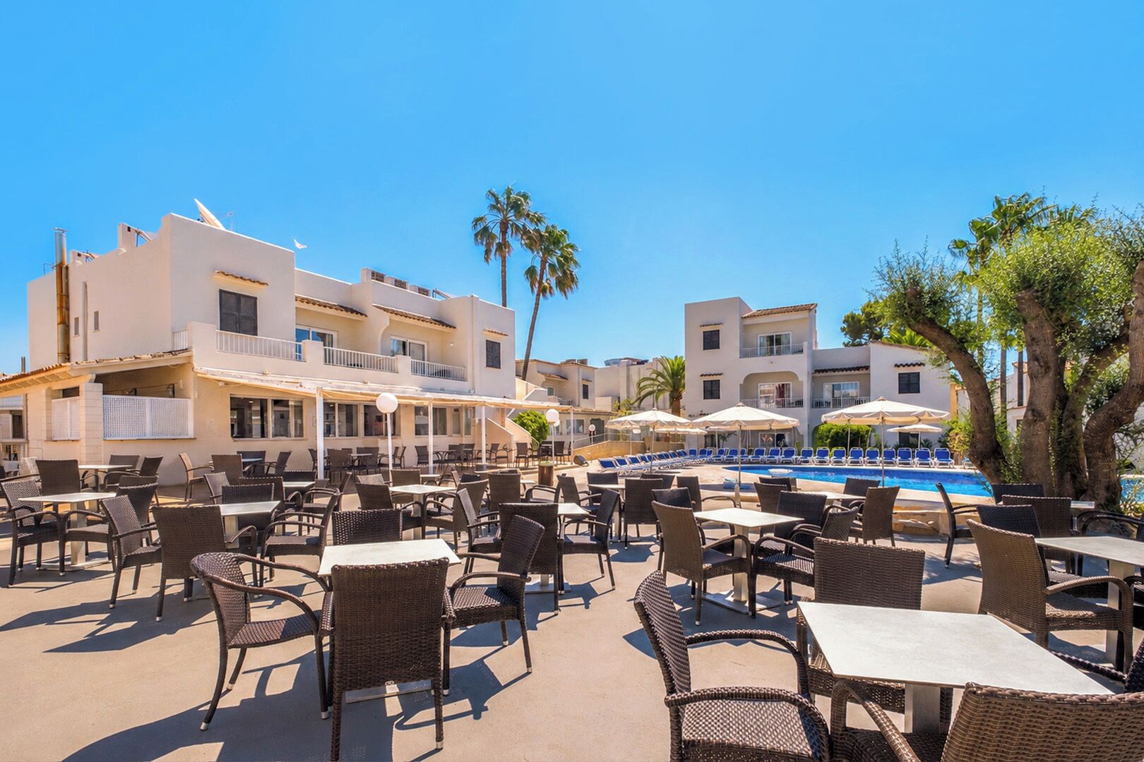 An outdoor pool area with lounge chairs and tables, surrounded by buildings with balconies.