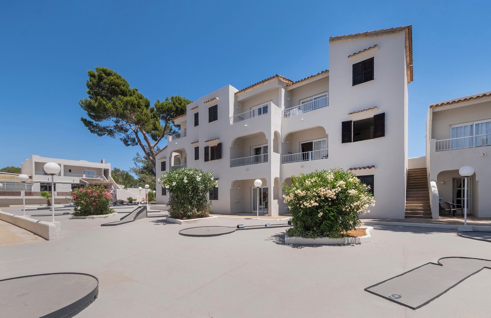 Un edificio residencial de varios pisos con balcones, un patio con jardineras y un cielo azul despejado.