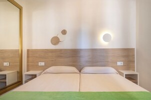 Habitación de hotel con una cama grande, mesitas de noche, un espejo y una lámpara fijada a la pared.