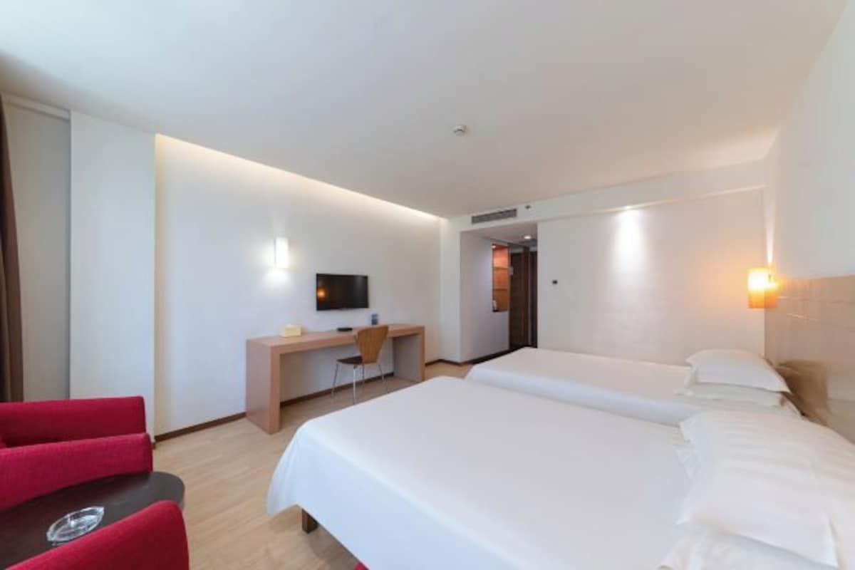 Una camera d'albergo con due letti, una scrivania, una TV e una sedia rossa.