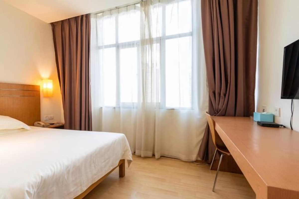Una camera d'albergo con un letto, una scrivania, una sedia, un comodino, una lampada e una televisione.
