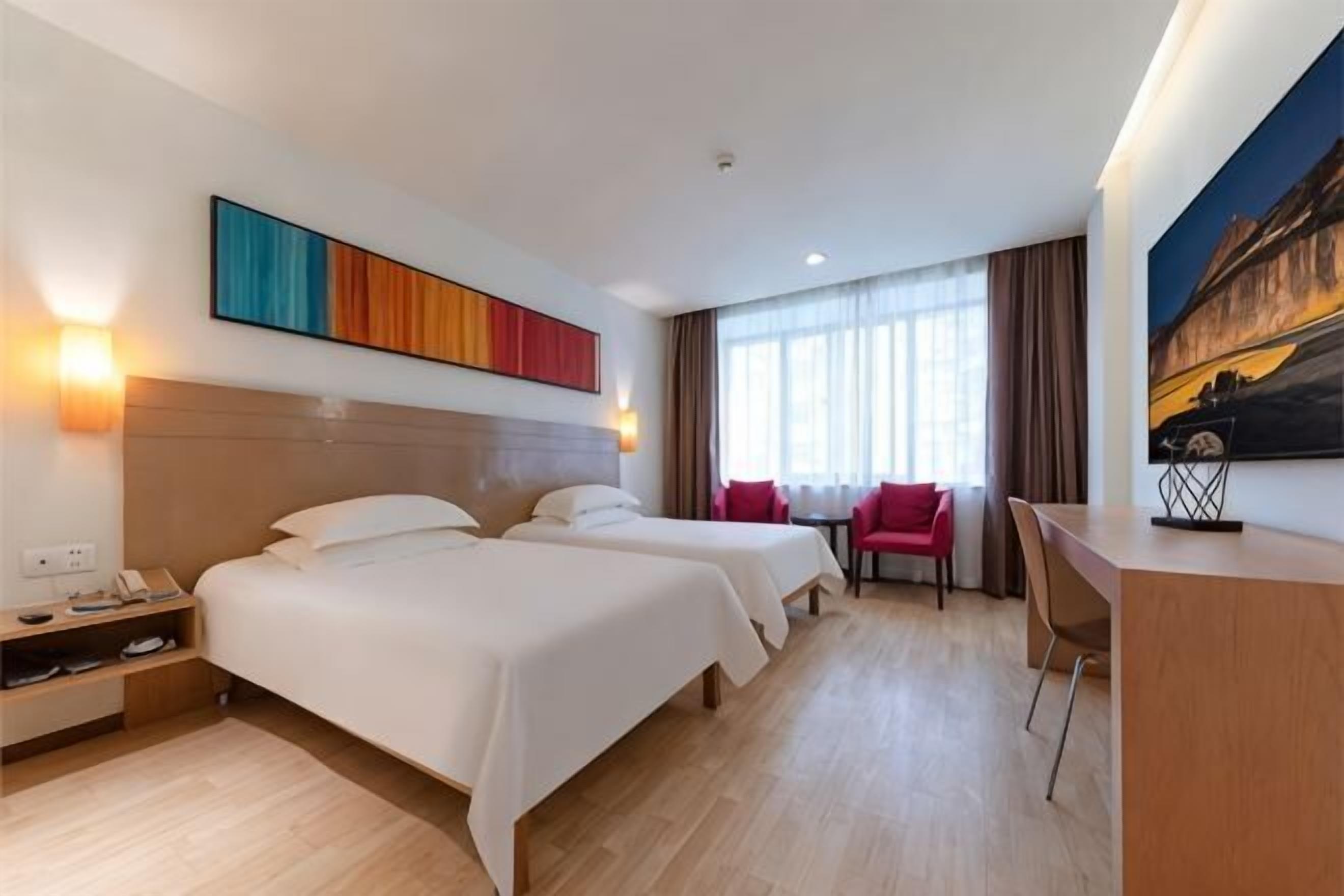 Ein Hotelzimmer mit zwei Betten, einem Schreibtisch, einem Stuhl und einem Gemälde an der Wand.