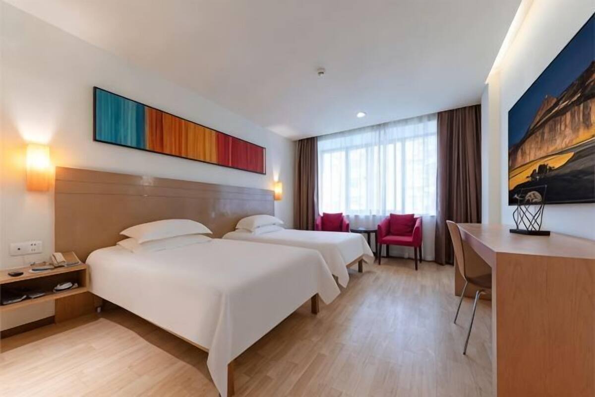 Ein Hotelzimmer mit zwei Betten, einem Schreibtisch, einem Stuhl und einem Gemälde an der Wand.