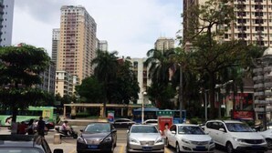 A parking lot with several cars parked, surrounded by tall buildings and trees.