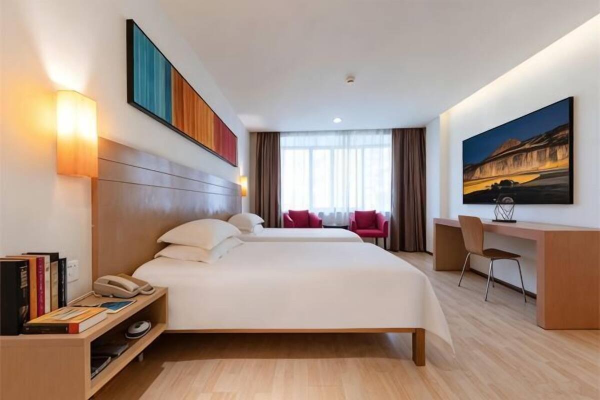 Ein Hotelzimmer mit zwei Betten, einem Schreibtisch, einem Stuhl, einem Bücherregal und einem Bild an der Wand.