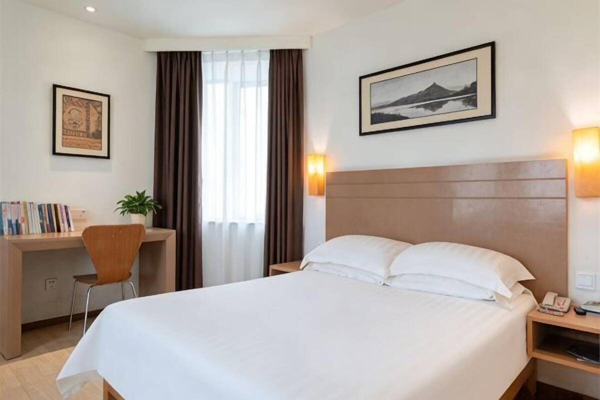 Ein Hotelzimmer mit Bett, Schreibtisch, Stuhl und Blick auf ein Gebäude durch das Fenster.