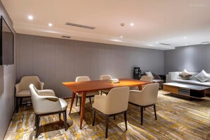 A modern hotel room with a wooden dining table, four chairs, a sofa, and a patterned carpet. - Ausotel New Tianhe Guangzhou (Guangzhou)
